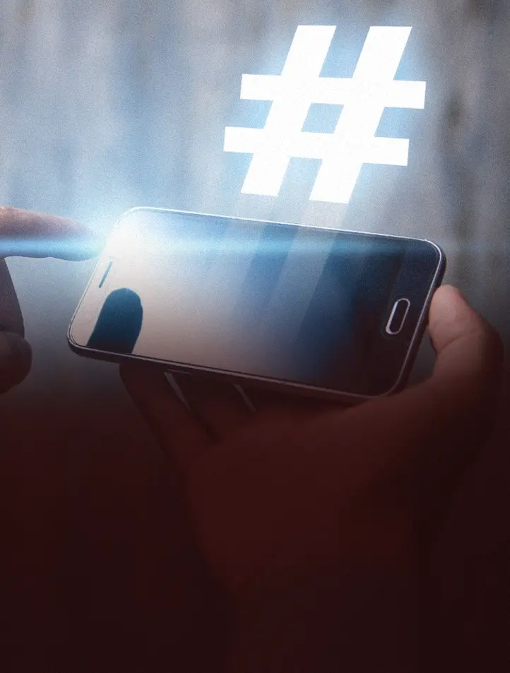 Mão segurando um celular com um símbolo de hashtag luminoso acima da tela